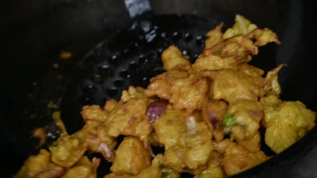 Onion pakora frying in iron pen. This is a popular street food in Indian subcontinent. Onion which are coated in seasoned&nbsp;spicy gram flour&nbsp;batter and deep fried. It originated in India.