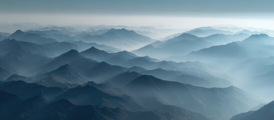 Misty, layered mountain range in shades of blue, viewed from a high vantage point, suggesting vastness and serenity