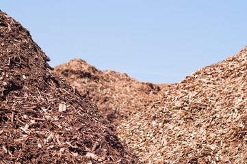 mountains of wood chips against the blue sky and green forest