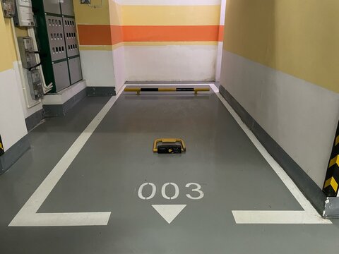 Underground parking space numbered 003 with ground parking barrier, wall-mounted electrical cabinets, and striped walls, in a clean and organized indoor parking lot setting.
