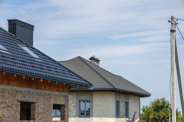 Two houses with distinct architectural styles are being built in an open countryside environment under a bright blue sky