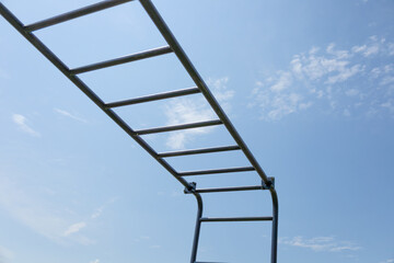 Children play on a monkey bar structure, enjoying a sunny afternoon under a bright blue sky and fluffy clouds