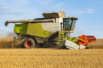 Obraz premium A large combine harvester works diligently to collect ripe crops in a sprawling golden field under a clear blue sky