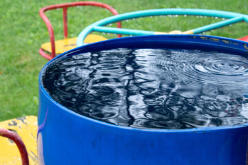 Blue, plastic water barrel reused for collecting and storing rainwater for watering plants full with water
