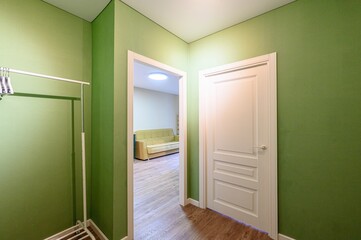interior shot shows a green hallway with a clothes rack. An open doorway reveals a room with a sofa. A closed white door is on the right