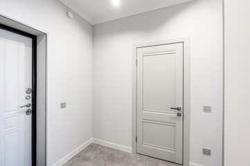 minimalist hallway featuring white walls, gray tile flooring, and two doors. One white door with a black frame, and a grey interior door