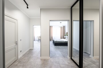 Hallway view leading to bedroom and dining area. Neutral tones, modern design with doors, mirrors, and tile floor