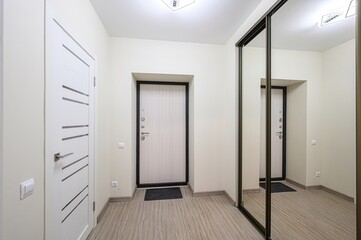 clean, modern hallway featuring three doors, a sliding mirror closet, and light wood flooring. Minimalist decor creates a bright, spacious feel
