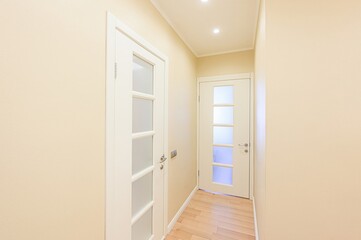 bright hallway with beige walls, light wood floors, and two white doors featuring frosted glass panels. Recessed lighting illuminates the space