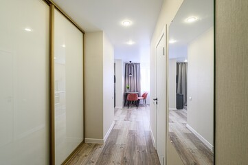 bright hallway features a sliding door wardrobe, a mirror, and a glimpse into a room with a small table and pink chairs. The floor has a wood grain pattern