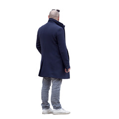 Homme chauve d’environ 40 ans vu de dos, debout, portant un manteau bleu marine, jean gris et baskets blanches, lunettes de soleil sur la tête, tenant un objet dans la main droite, journée fraiche. 
