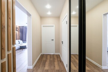 modern hallway with wooden floors, beige walls, white doors, recessed lighting, and a full-length...