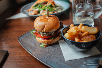 Restaurant burger with beef patty lettuce tomato and cheese served with golden chips and glass of water. Dublin pub food presentation on dark wooden table.