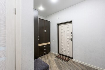 Entryway with a wardrobe, front door, and patterned wood floors. The walls are painted white. There's a bench near the closet