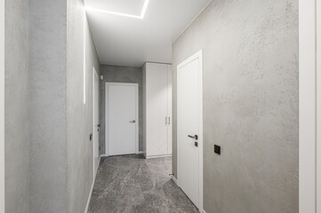 modern hallway with gray textured walls, white doors, and geometric lighting. The floor is gray marble tile