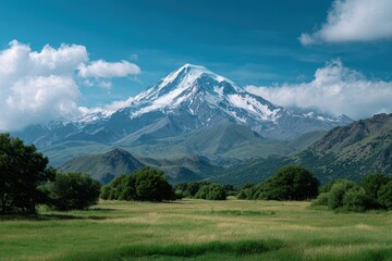 Majestic snow capped mountain peak under a vibrant blue sky with fluffy clouds and green rolling hills below
