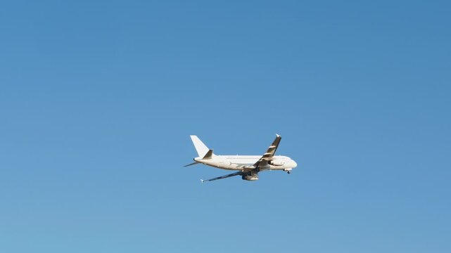 Commercial airplane in low flight against a clear blue sky, viewed from below at an angle, with landing gear extended during ascent or approach. Taking off, altitude gain, flying over, airport. 