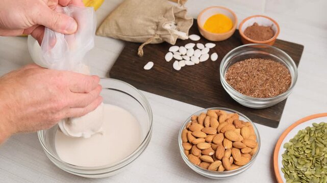 Male hands use filtering culinary cheesecloth bag for squeezing ground almonds and making almond milk using blender. Homemade plant base for vegan smoothies and cocktails as alternative to cow milk.