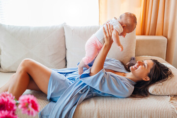 Young mother playing with newborn baby during tummy time at home. Infant looks at fold-out interactive high contrast book