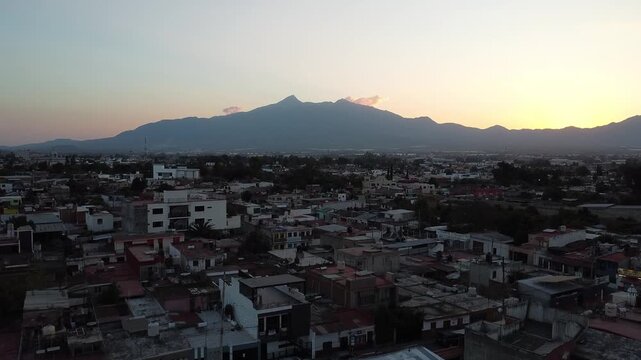 Drone footage over Ciudad Guzman city during sunset, in front of the nevado de colima volcano