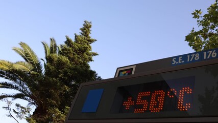 Madrid. Spain. A digital thermometer mounted on a bus stop shelter alternates between the local time (19:49) and a staggering temperature of 50 degrees Celsius. 