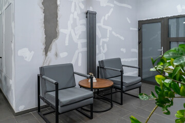 Contemporary waiting room featuring modern grey armchairs, round wooden side table, and tall...