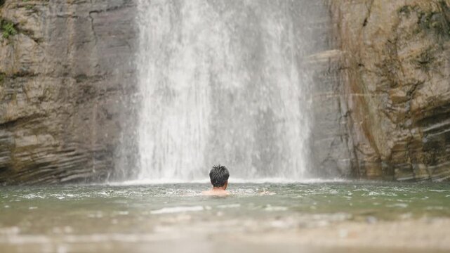 Playful Indian boy standing under falling water, eyes closed with joy.