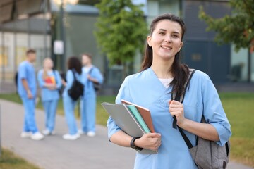 Fototapeta premium Medical student in uniform with backpack and notebooks outdoors, selective focus