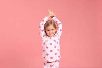 Cute little girl in pajamas on pink background