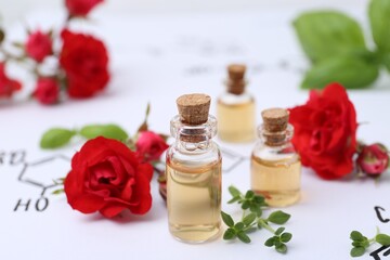 Bottles of cosmetic products, herbs and red roses on paper with chemical formulas, closeup