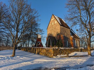 Medieval stone church with snow covered ground and bare trees against a blue sky