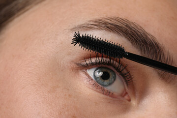 Obraz premium Young woman applying mascara onto her eyelashes, closeup