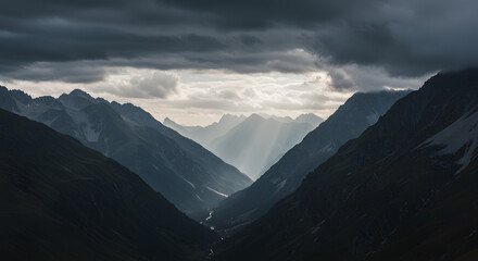 Obraz premium Epic vista of a mountain valley shrouded in moody clouds and pierced by radiant light streams, evoking a sense of vastness and serene grandeur with peaks layered in atmospheric perspective
