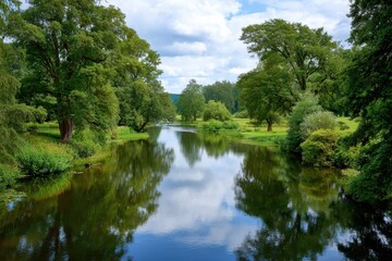 Fototapeta premium Serene river reflecting lush green trees and cloudy sky on a sunny day