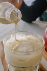 Deliciously refreshing close-up of a hand pouring rich espresso over milk and ice in a clear glass, creating a perfect iced latte