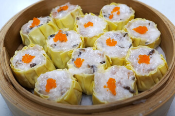 Top view of freshly steamed siu mai dumplings topped with bright orange fish roe in a bamboo steamer basket.

