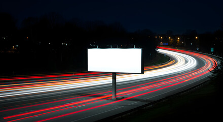 A blank white billboard for advertising stands next to a busy highway at night with long exposure light trails.