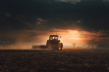 A farmer works hard until sunset in a field with a tractor.