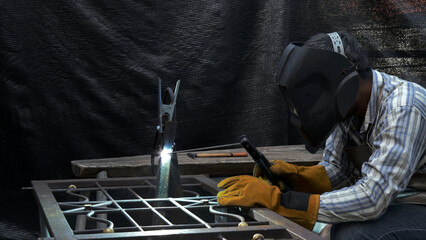 Focused welder wearing protective mask and gloves working on detailed metal framework with electric...