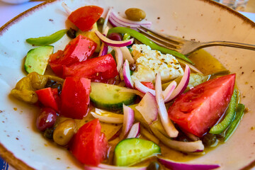 Fresh Greek salad with tomatoes, cucumbers, red onions, green peppers, olives, and feta cheese, drizzled with olive oil and served on a ceramic plate.
