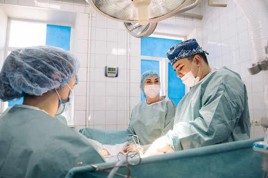 Surgical team in operating room, focused on procedure, wearing scrubs and masks, with bright lighting and medical equipment, showcasing teamwork and precision in a critical healthcare environment