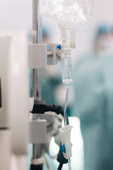 Intravenous drip setup in a surgical environment, showcasing clear fluid flow through tubing, with blurred medical personnel in scrubs and surgical instruments in the background