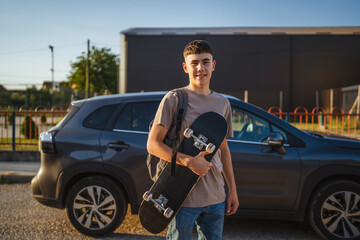 Young skater holding his skateboard is posing in front of his car in a parking lot © Miljan Živković