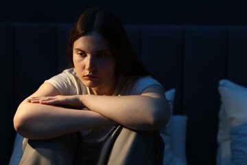 Sad young woman sitting on bed at home