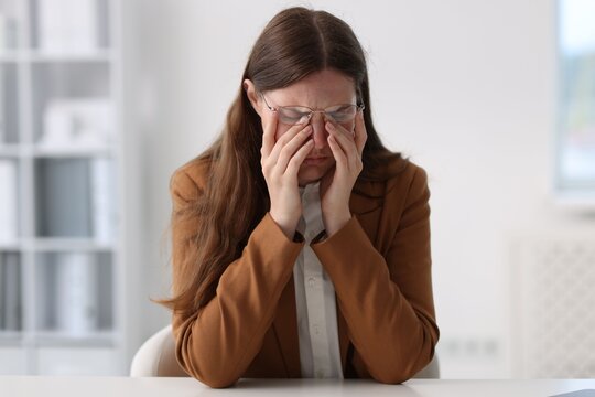 Sad young woman at white table in office