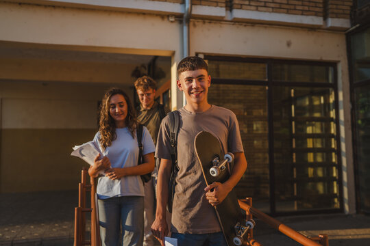 Students leaving school at sunset holding skateboard and books