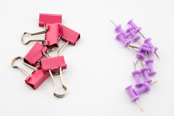 Pink binder clips and purple push pins arranged on a white background. Colorful stationery composition highlighting metallic textures and vibrant colors.