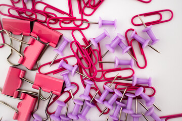 Red paper clips and purple push pins scattered on a white background, with a pink binder clip partially visible. A colorful stationery mix for office, school, and organization themes.