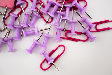 Red paper clips and purple push pins scattered on a white background, with a pink binder clip partially visible. A colorful stationery mix for office, school, and organization themes.