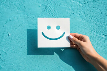 Positive Vibes Hand Holding Smiley Face Cutout Against a Vibrant Blue Wall Expressing Happiness and Joy